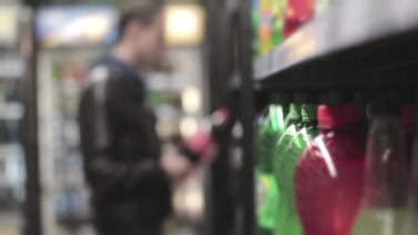 Man takes a bottle of soda off of the shelf in a convenience store