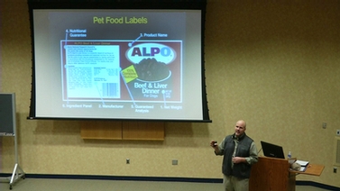 Dr. Joseph J. Wakshlag stands near a projector screen showing an Alpo pet food label