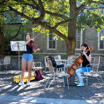One student playing a violin with an another student playing cello next to them on Ho Plaza.