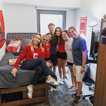 A group of people smiling in a dorm room during move-in. 