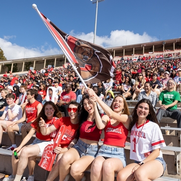 Students smiling and waving Cornell flag during Homecoming weekend