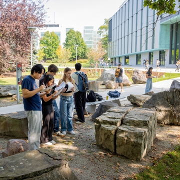 A group of Cornell students during class by the Engineering quad in front of large boulders.