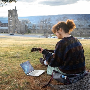 a female student plays music under a tree on libe slope at cornell university