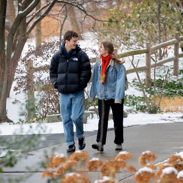 Two Cornellians conversing on a snowy path surrounded by winter foliage at Cornell University.