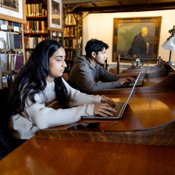 Two students using their laptops in the library. 