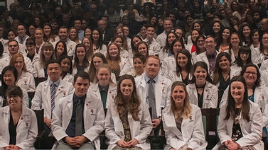 Students in white coats look at the camera.