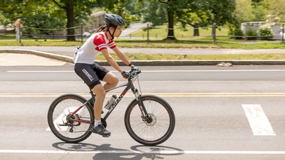 A person wearing Cornell bike gear, bikes through campus. 